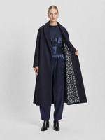 Load image into Gallery viewer, A model stands against a light gray studio background wearing a long dark navy coat over a matching navy outfit, with the coat open to show a patterned lining.