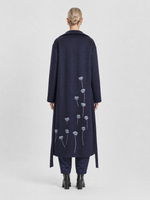Load image into Gallery viewer, A model viewed from the back wearing a long navy coat with embroidered white poppy flowers on the back, paired with navy trousers and black boots, against a light gray studio background.
