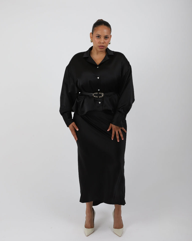 Woman wearing a black silk shirt over a black slip dress with a silver belt